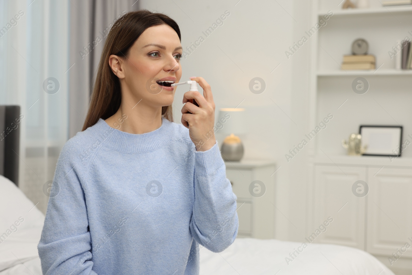 Photo of Adult woman using throat spray in bedroom, space for text