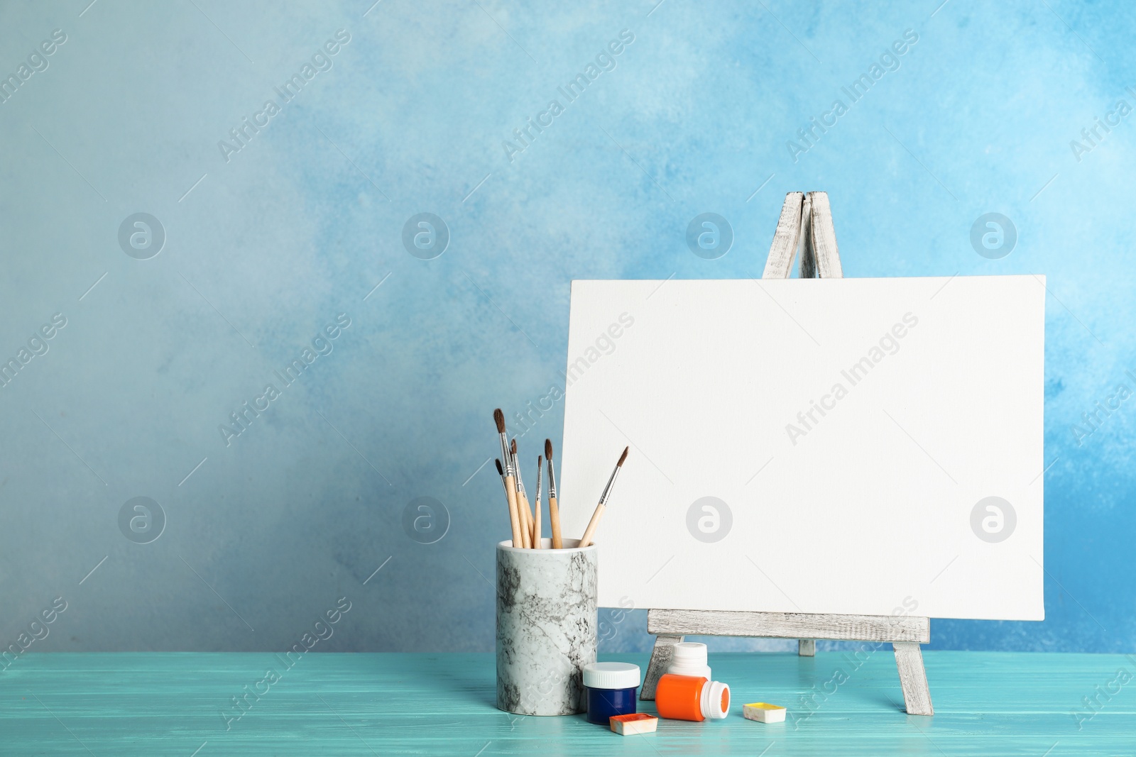 Photo of Wooden easel with blank canvas board and painting tools for children on table near color wall. Space for text