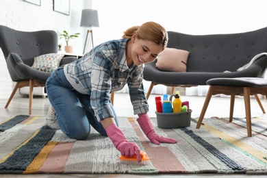 Photo of Portrait of woman cleaning carpet with brush in living room