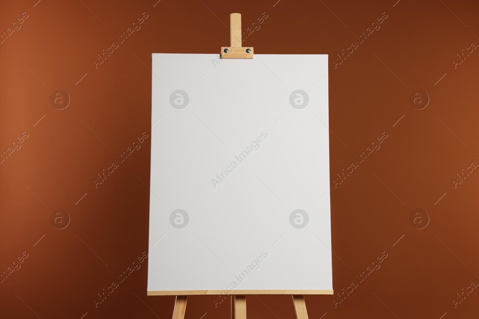 Photo of Wooden easel with blank canvas on brown background