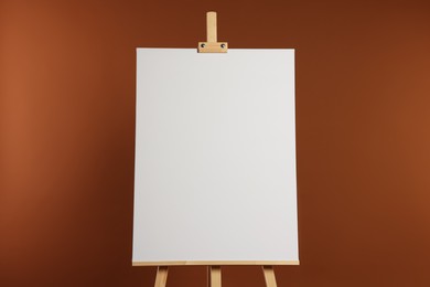 Photo of Wooden easel with blank canvas on brown background