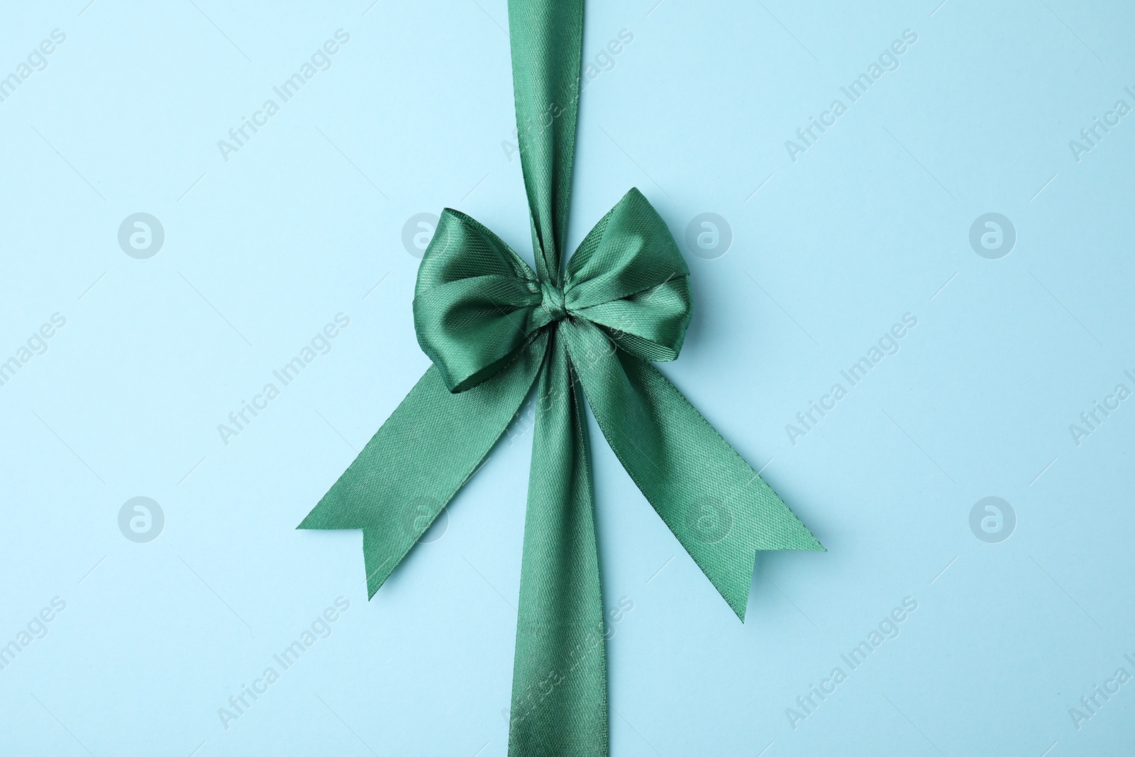 Photo of Green satin ribbon with bow on light blue background, top view