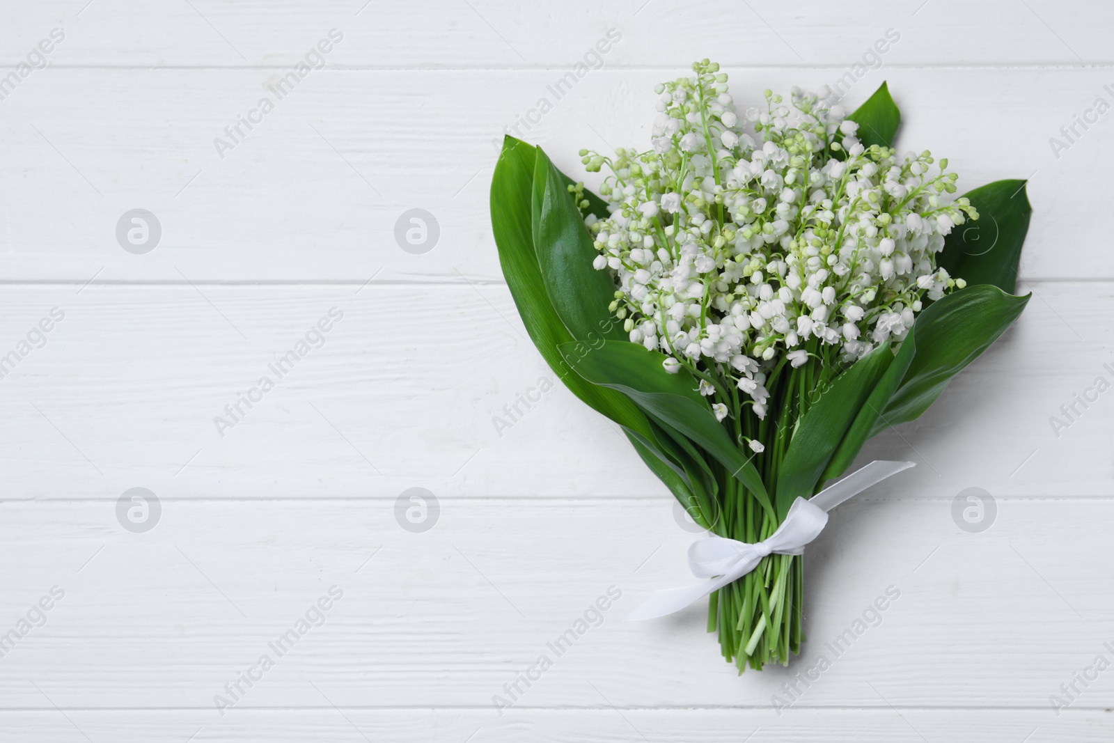 Photo of Beautiful lily of the valley flowers on white wooden table, top view. Space for text