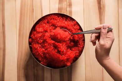 Photo of Woman holding spoon with fresh red caviar at wooden table, top view