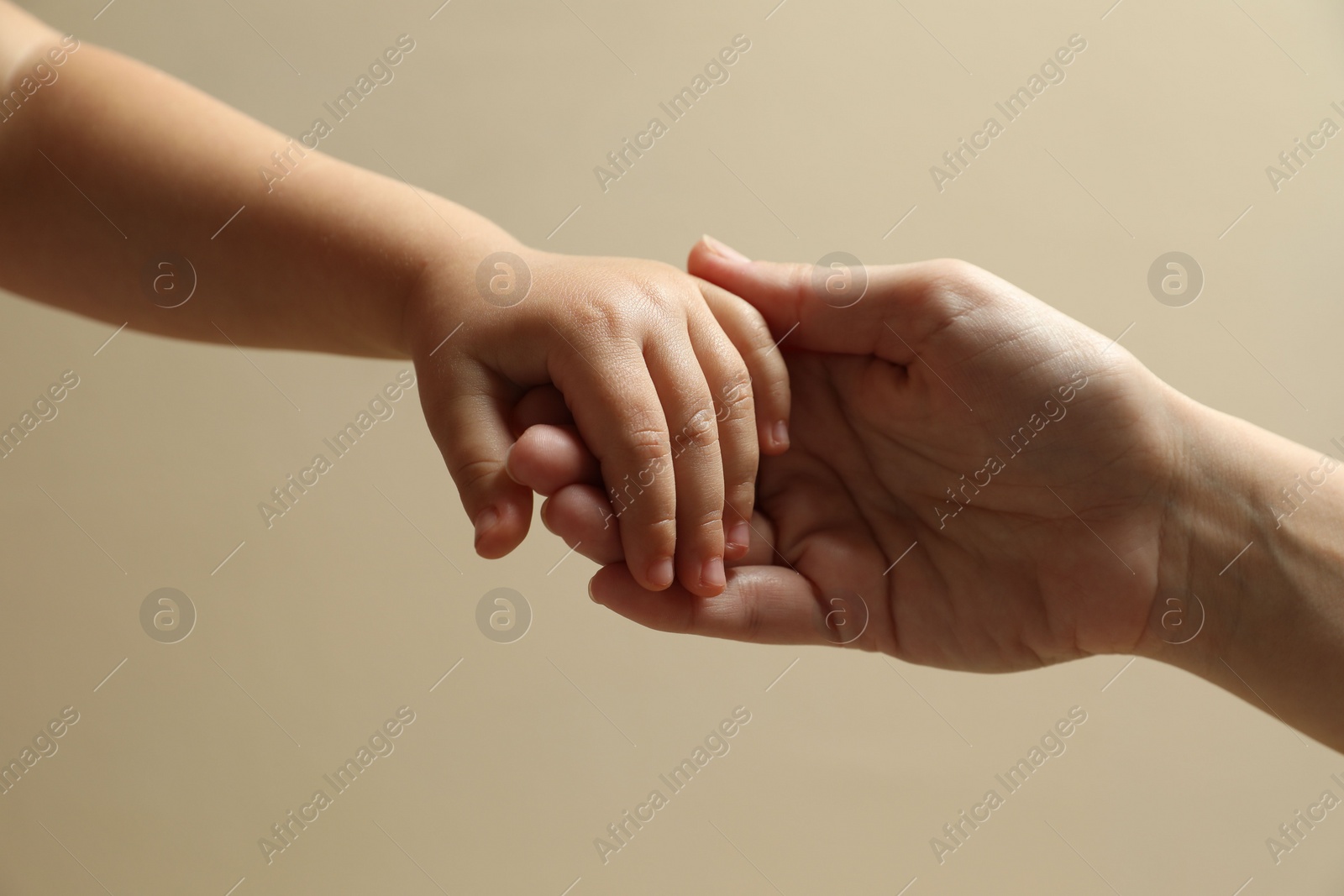 Photo of Mother and child holding hands on beige background, closeup