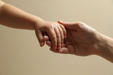 Photo of Mother and child holding hands on beige background, closeup