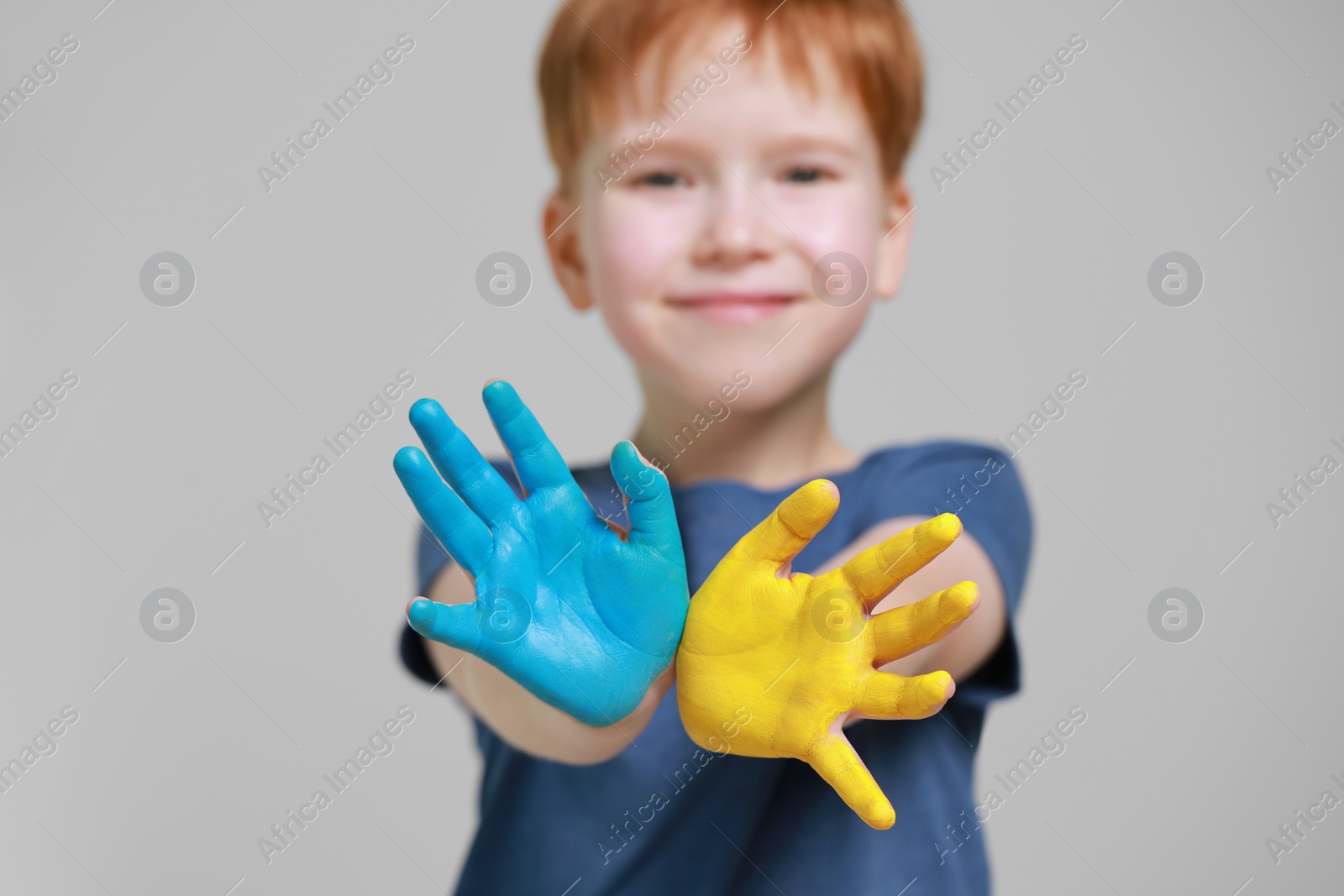 Photo of Little boy with hands painted in Ukrainian flag colors against light grey background, focus on palms. Love Ukraine concept