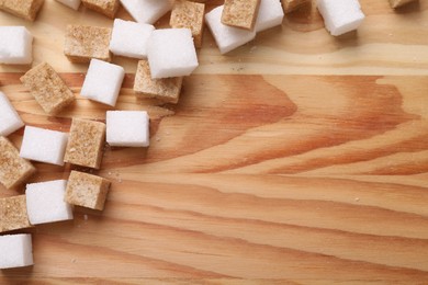 Photo of White and brown sugar cubes on wooden table, flat lay. Space for text