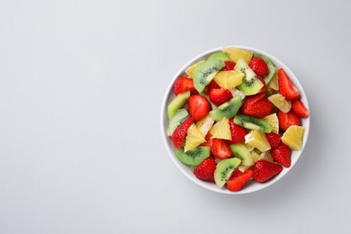 Photo of Yummy fruit salad in bowl on light grey background, top view. Space for text