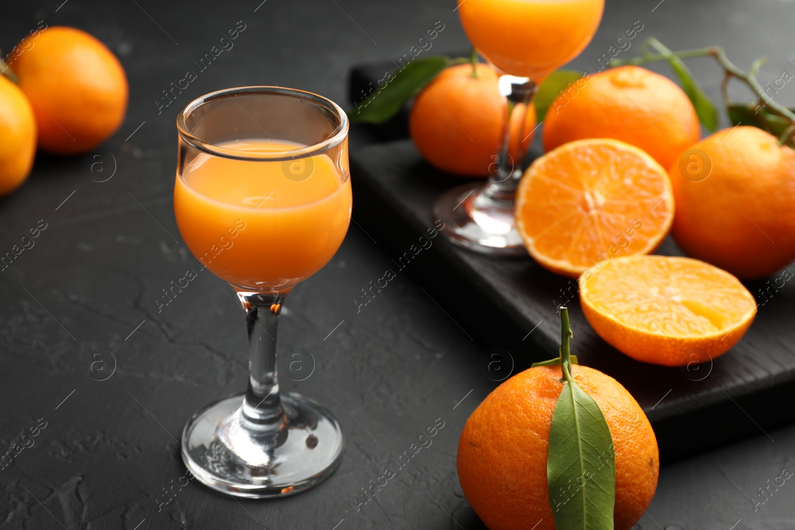 Photo of Tasty tangerine liqueur in glasses and fresh citrus fruits on black textured table