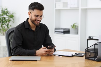 Photo of Handsome young man using smartphone at wooden table in office