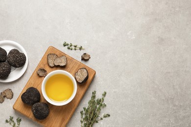 Photo of Fresh truffles, oil in bowl and thyme on light grey table, flat lay. Space for text