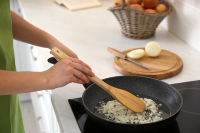 Photo of Woman frying chopped onion in kitchen, closeup
