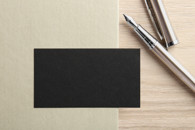 Photo of Blank black business card, fountain pen and notebook on wooden table, top view. Mockup for design