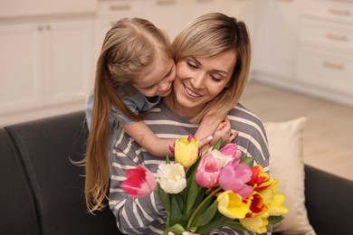 Photo of Little daughter congratulating her mom with Mother`s Day at home. Woman holding bouquet of beautiful tulips