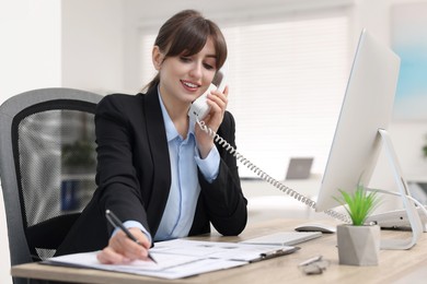 Smiling secretary talking on telephone at table in office