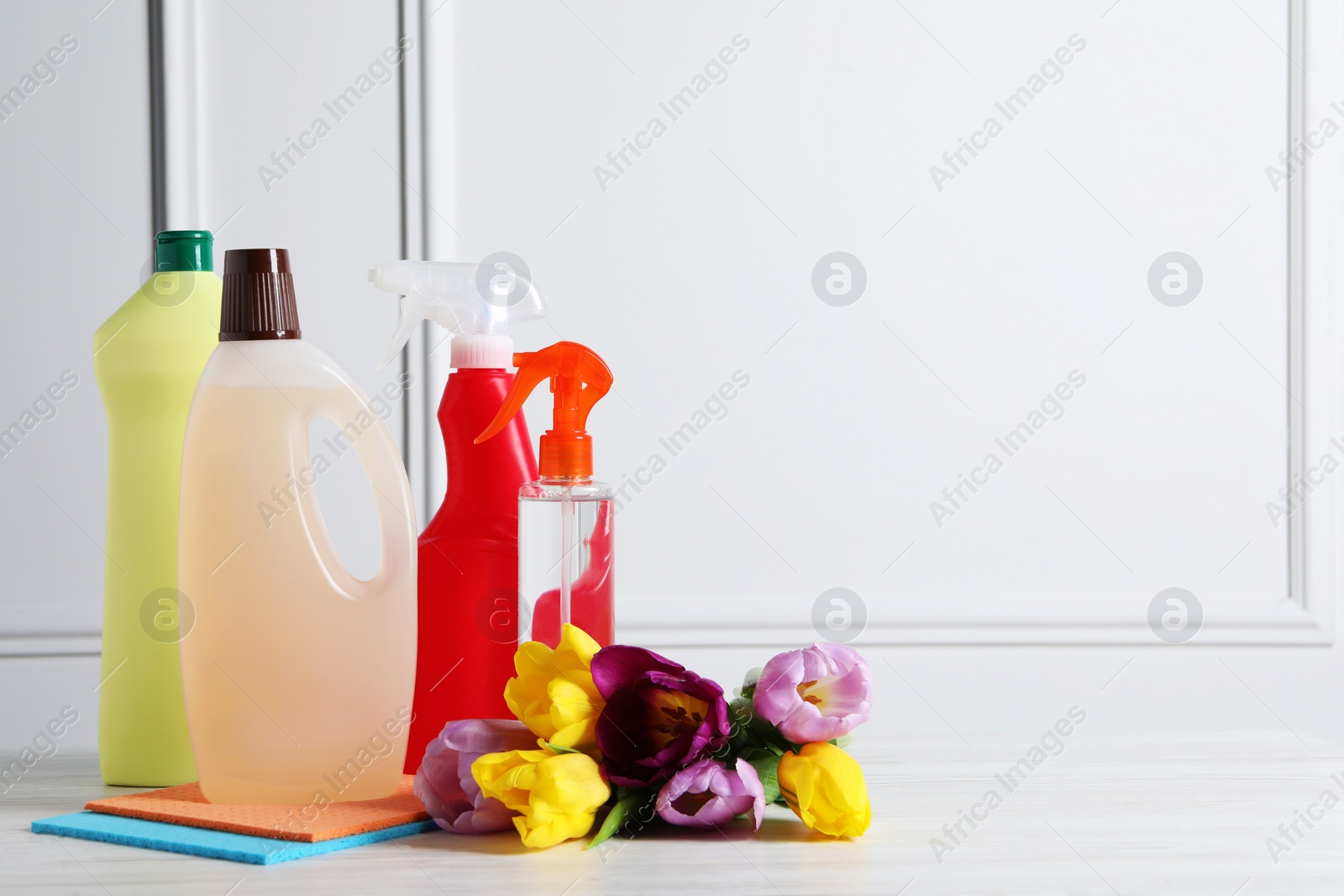 Photo of Spring cleaning. Detergents, flowers and rags on white wooden table. Space for text