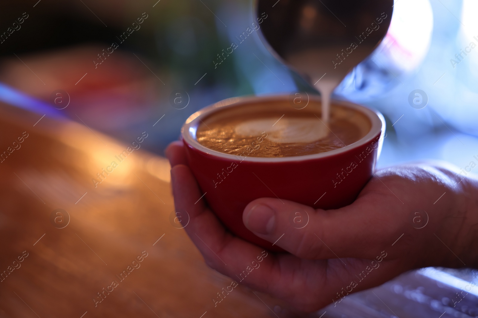 Photo of Barista pouring milk into cup of coffee over table, closeup