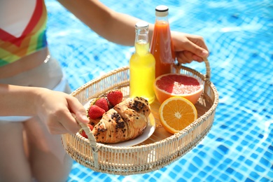 Photo of Young woman with delicious breakfast on tray in swimming pool, closeup