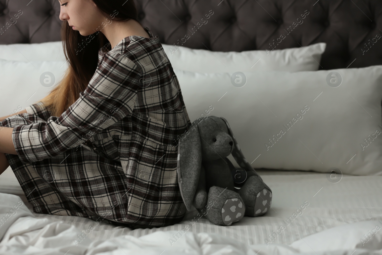 Photo of Upset teenage girl with toy sitting on bed. Space for text