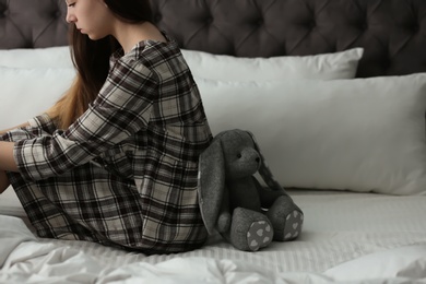 Upset teenage girl with toy sitting on bed. Space for text