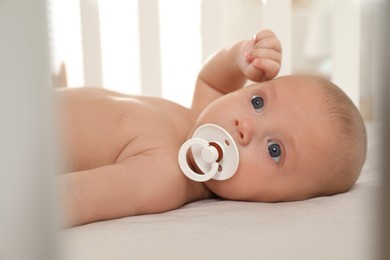 Photo of Cute little baby with pacifier lying in crib