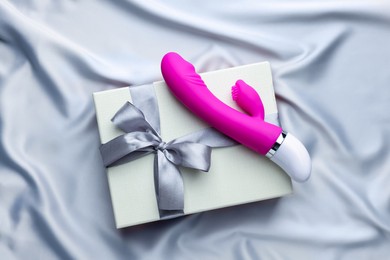 Photo of Gift box and pink vaginal vibrator on grey silk fabric, top view. Sex toy
