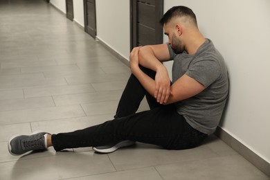 Photo of Sad man sitting on floor in hall. Space for text