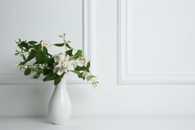 Photo of Beautiful bouquet with fresh jasmine flowers in vase on white table indoors, space for text