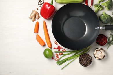 Empty iron wok surrounded by raw ingredients on white wooden table, flat lay. Space for text