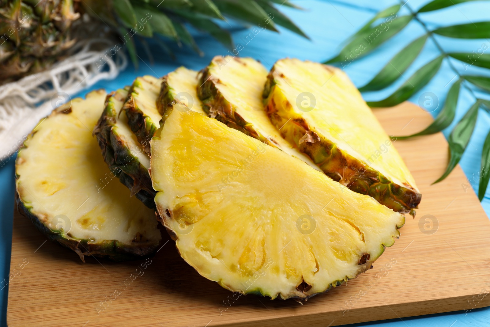 Photo of Slices of ripe juicy pineapple and green leaf on light blue table, closeup