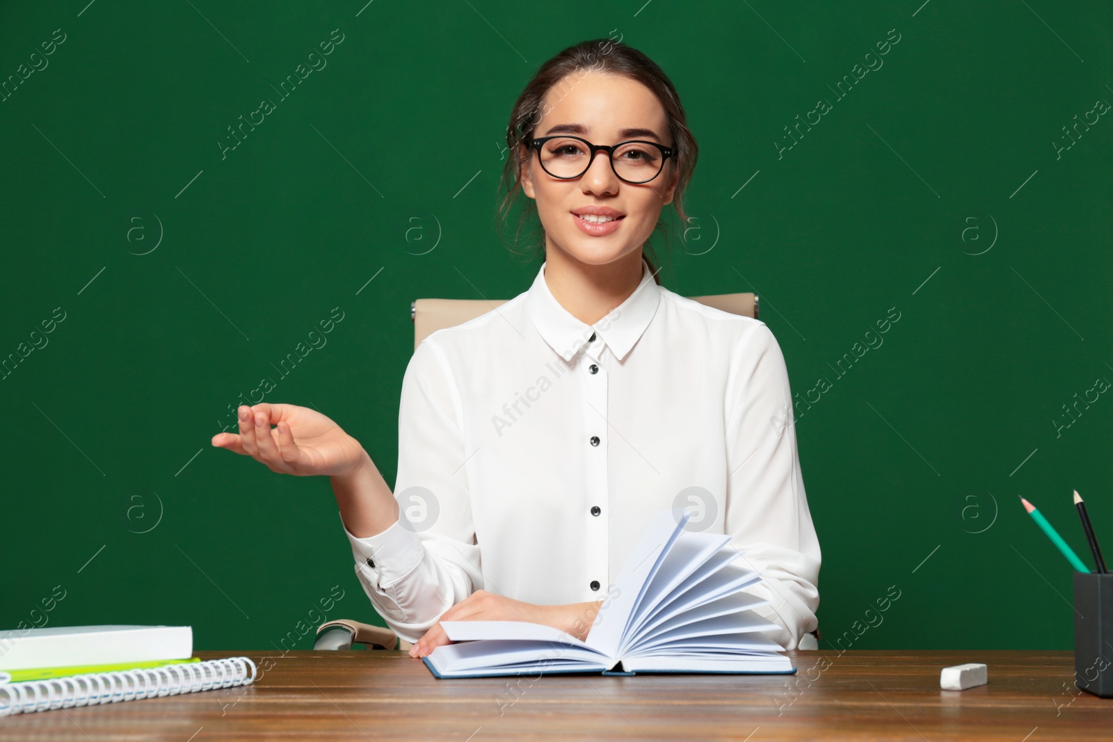 Photo of Portrait of beautiful young teacher sitting at table near chalkboard