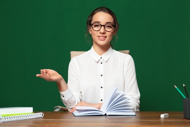 Photo of Portrait of beautiful young teacher sitting at table near chalkboard