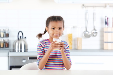 Adorable African-American girl with glass of milk in kitchen