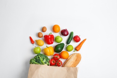 Paper bag with different groceries on white background, top view