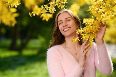 Beautiful young woman near blossoming shrub on spring day, space for text