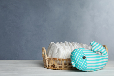 Tray with baby diapers and toy on white wooden table against grey background. Space for text