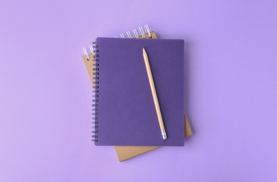 Notebooks with pencil on lilac background, top view