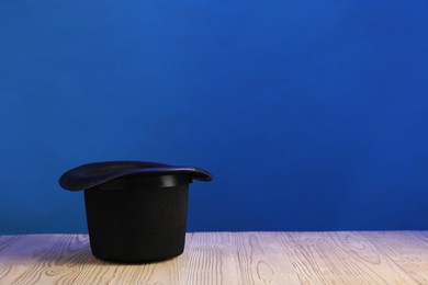 Photo of Magician's hat on wooden table against blue background, space for text