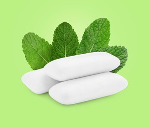 Menthol chewing gum pillows and mint leaves on light green background