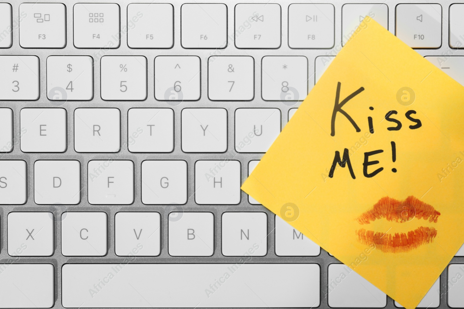 Photo of Sticky note with phrase Kiss Me and lipstick mark on keyboard, top view