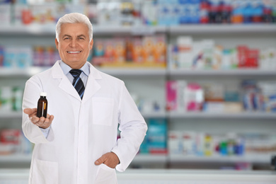 Professional senior pharmacist with syrup in modern drugstore, space for text 