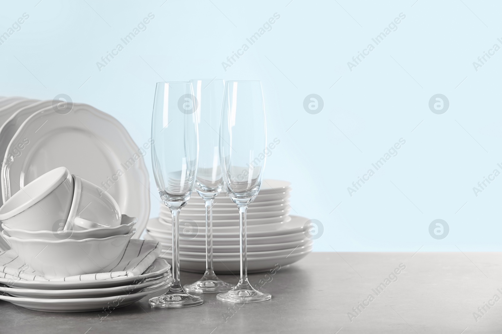 Photo of Set of clean dishes on table against light background. Space for text