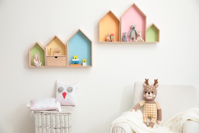 Stylish baby room interior design with house shaped shelves and comfortable armchair