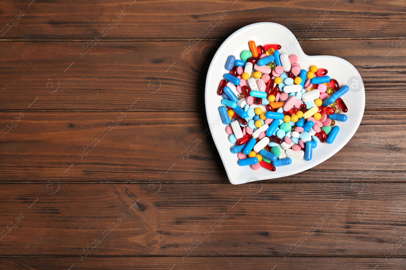 Photo of Heart shaped plate with different pills on wooden background. Cardiology concept