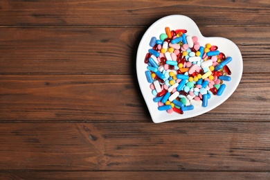 Heart shaped plate with different pills on wooden background. Cardiology concept