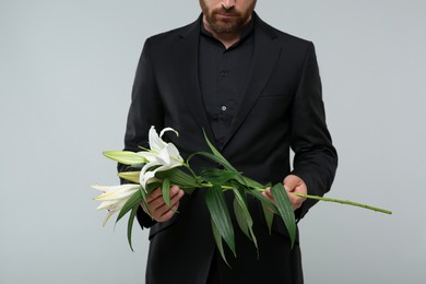 Man with white lilies on light grey background, closeup. Funeral ceremony