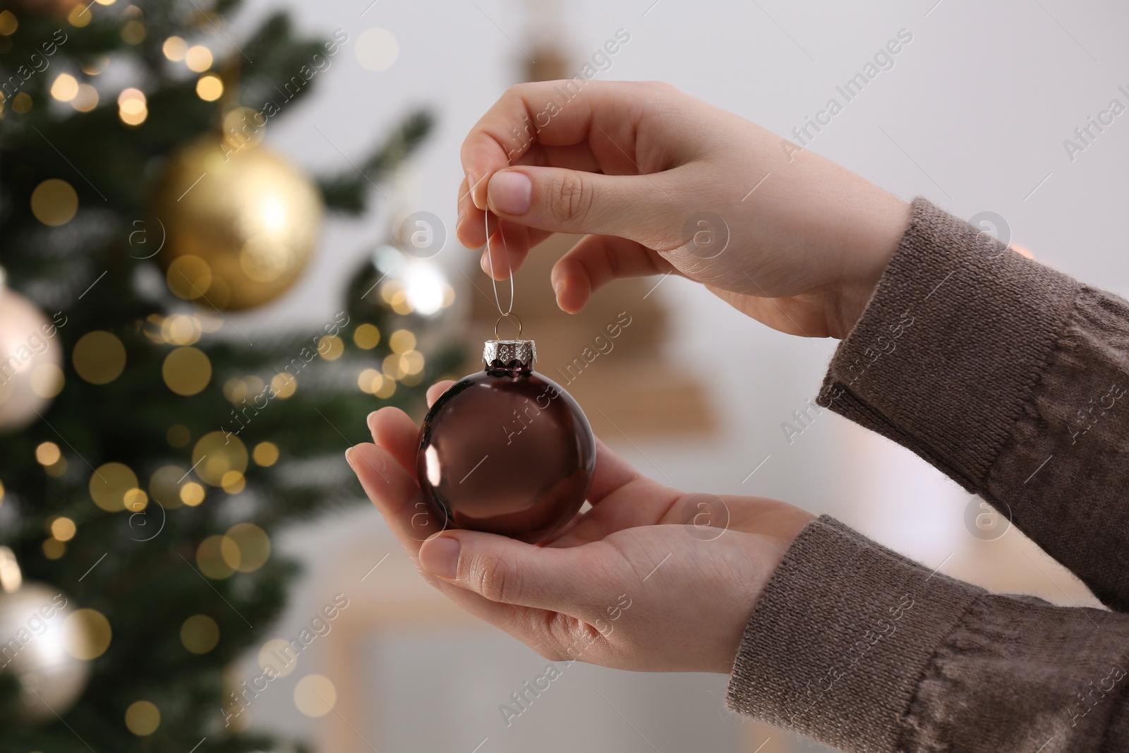 Photo of Woman holding brown ball near Christmas tree indoors, closeup