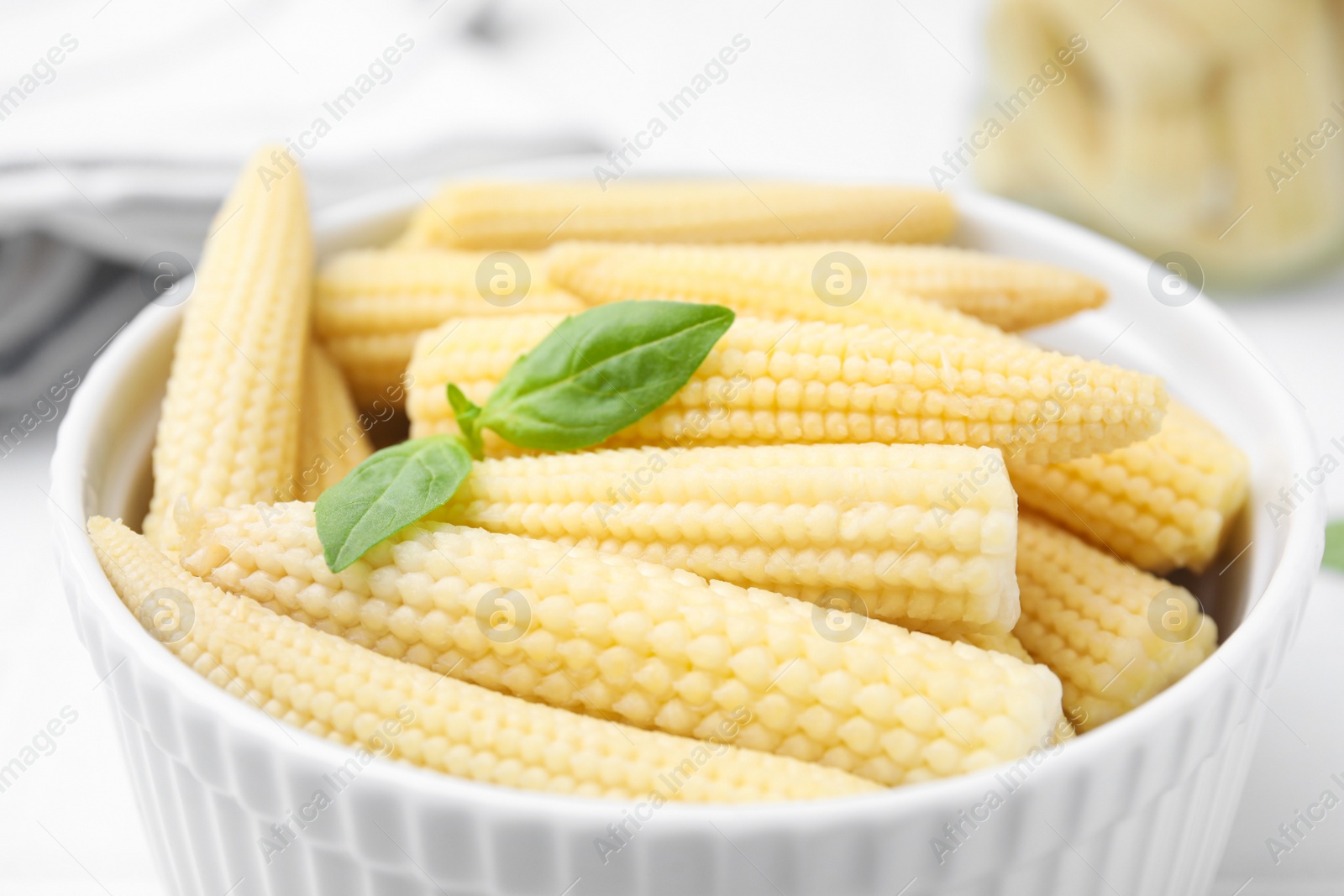 Photo of Canned baby corns with basil on white table, closeup