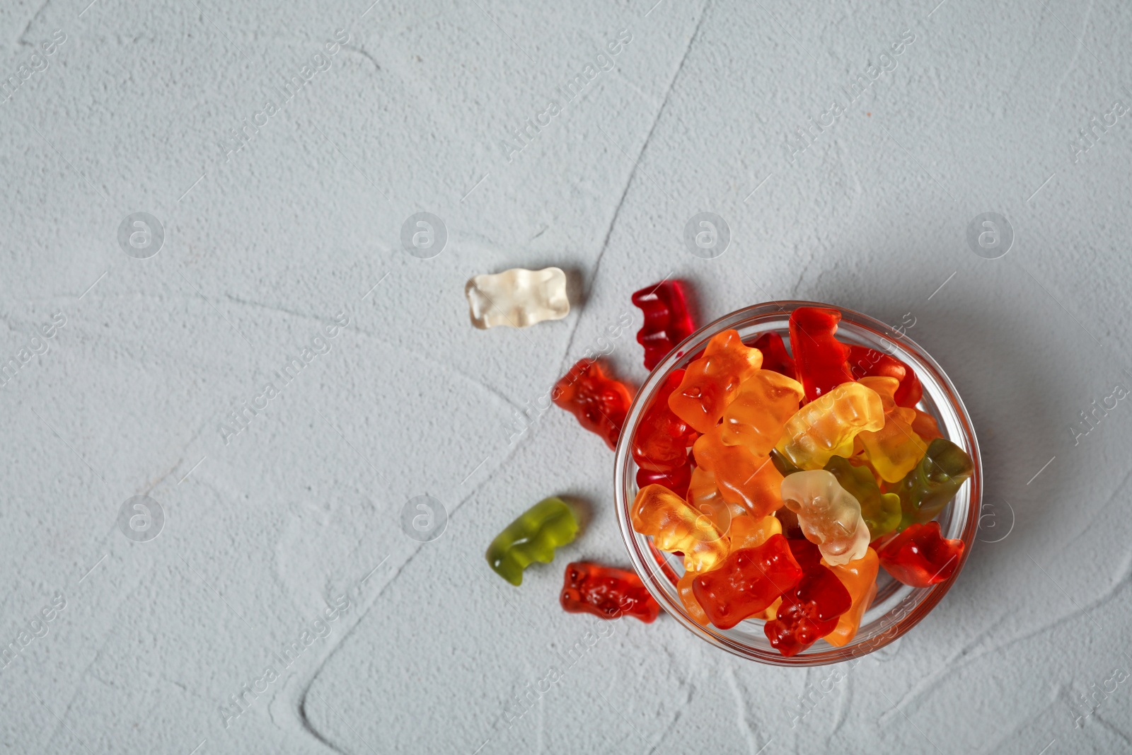 Photo of Bowl with delicious jelly bears on grey table, flat lay. Space for text